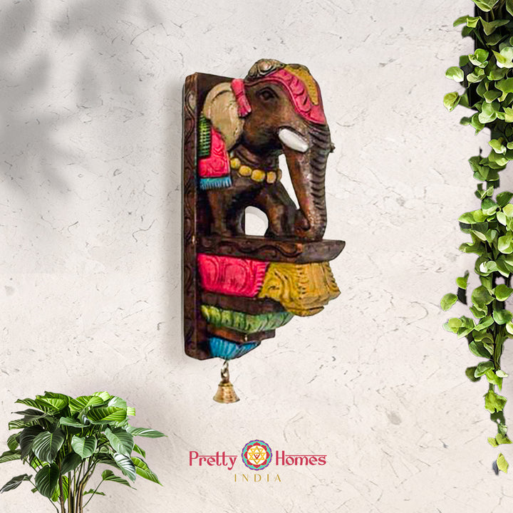 Hand-painted multicolored wooden elephant wall sconce with carved saddle and small hanging brass bell.
