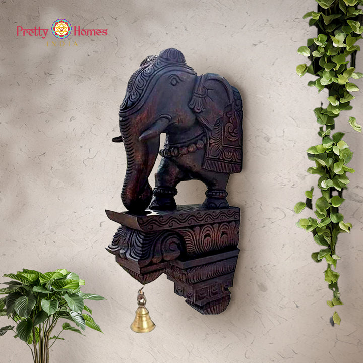 Hand-carved wooden elephant corbel with ornate base and hanging brass bell.