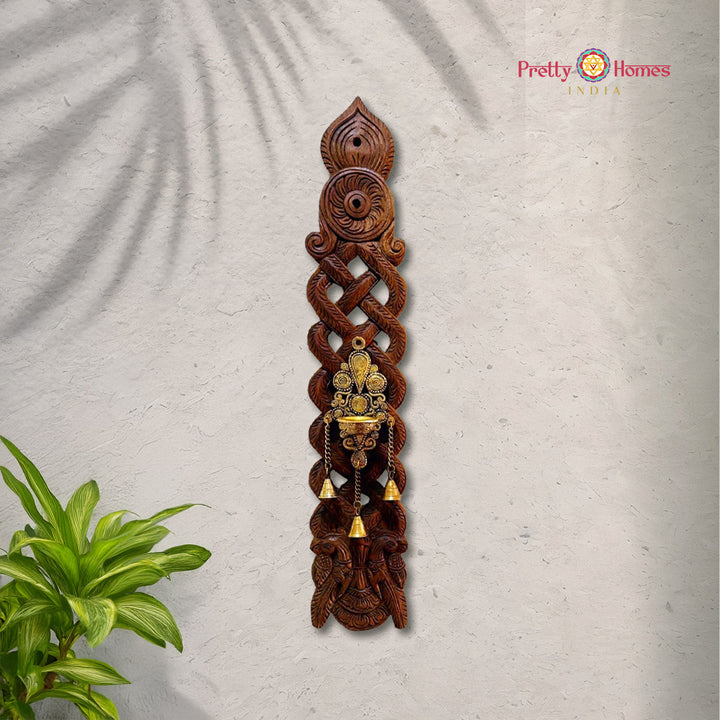 Tall intricately carved wooden wall panel with brass hanging lamp and multiple small brass bells.