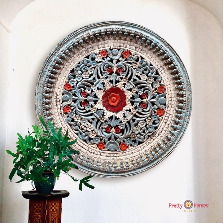 A hand-carved wooden jali wall panel with a distressed painted finish in blue, white, and red, mounted on a wall.