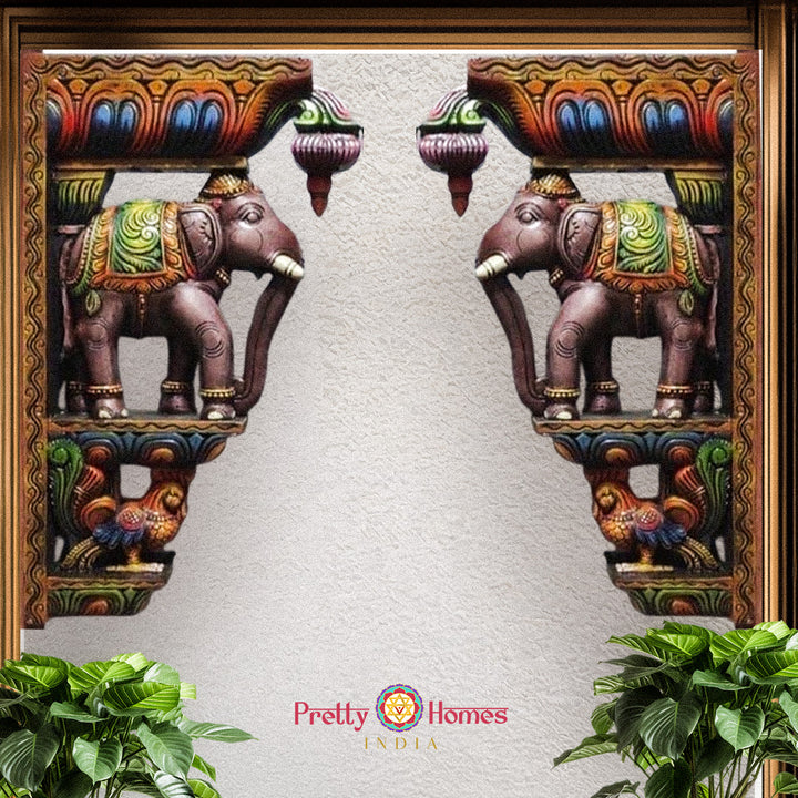 Pair of colourfully painted wooden elephant corbels with peacock accents in decorative frame.