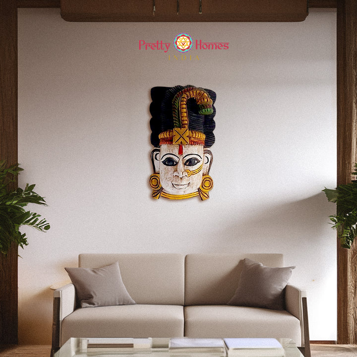 Decorative hand-painted wooden deity head mask with multicolour crown, staged on living room wall.