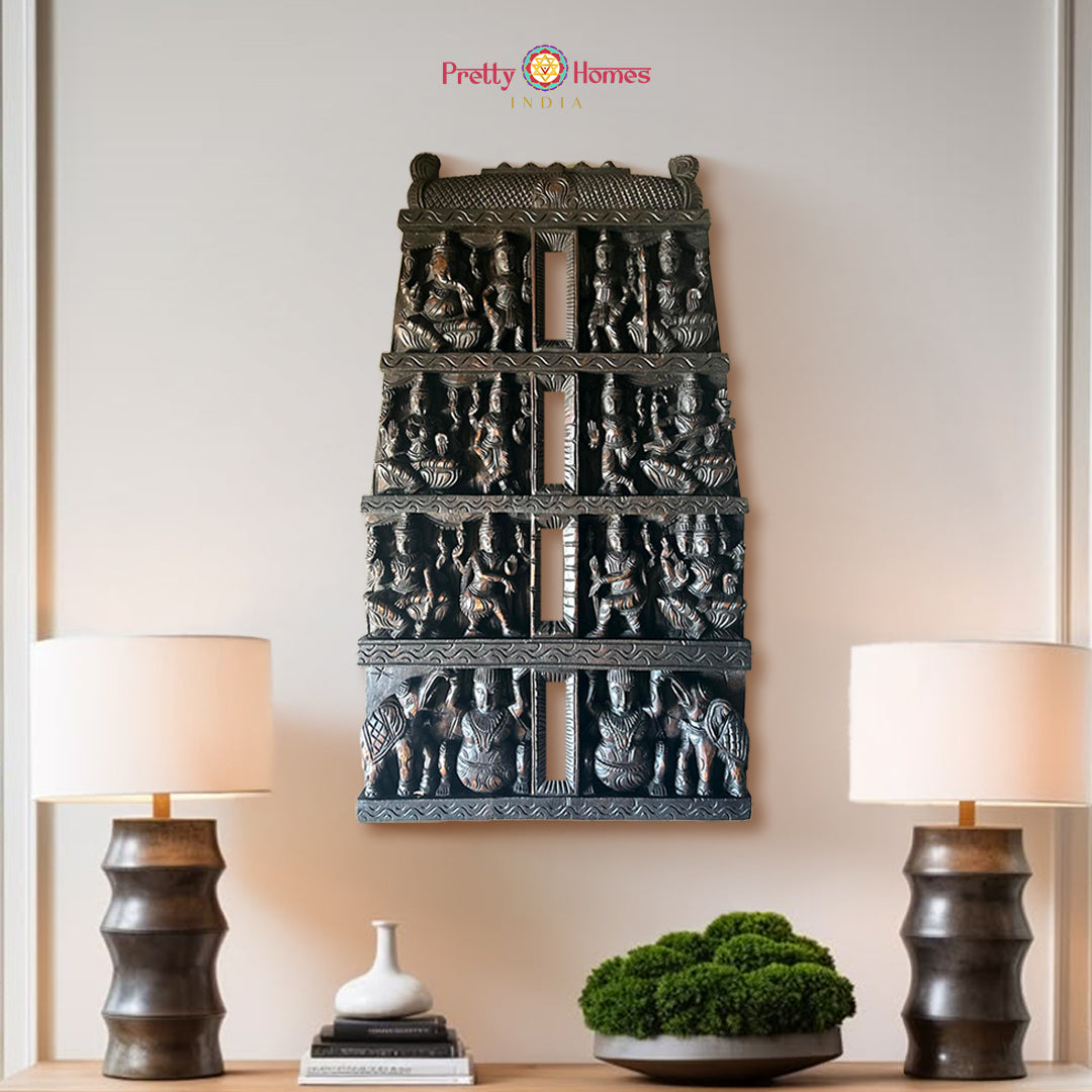 Antique style teak wood Temple Gopuram wall panel with various god figures in relief, handcarved with intricate details, displayed between two lamps on a wall.
