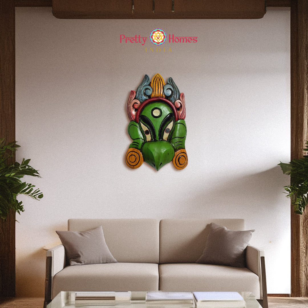 Decorative green painted wooden mask with bird-like features, shown mounted above sofa.