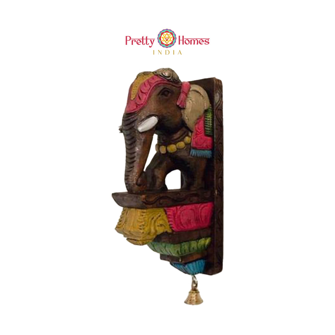 Side view of a painted wooden elephant wall shelf showing carved details and a tiny hanging bell.