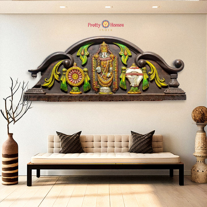 Decorative wall piece above a sofa with 'Pretty Homes' branding. Horizontal wooden wall panel with Tirupati Balaji, Shankh, Chakra, and floral motifs


