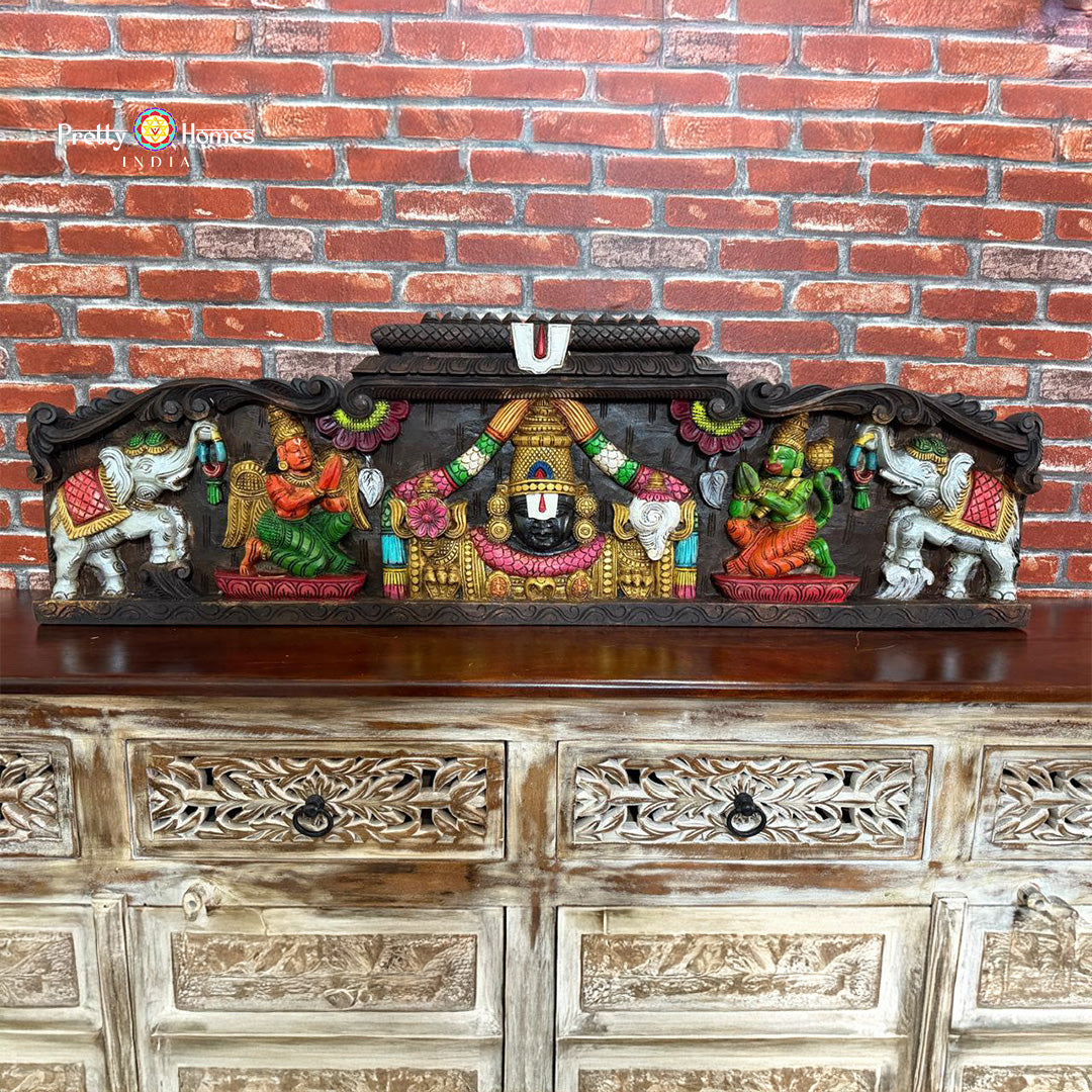 Decorative wall art with colorful figures on a wooden cabinet against a brick wall - Hand-carved Vagai wood wall panel in temple Gopuram style
