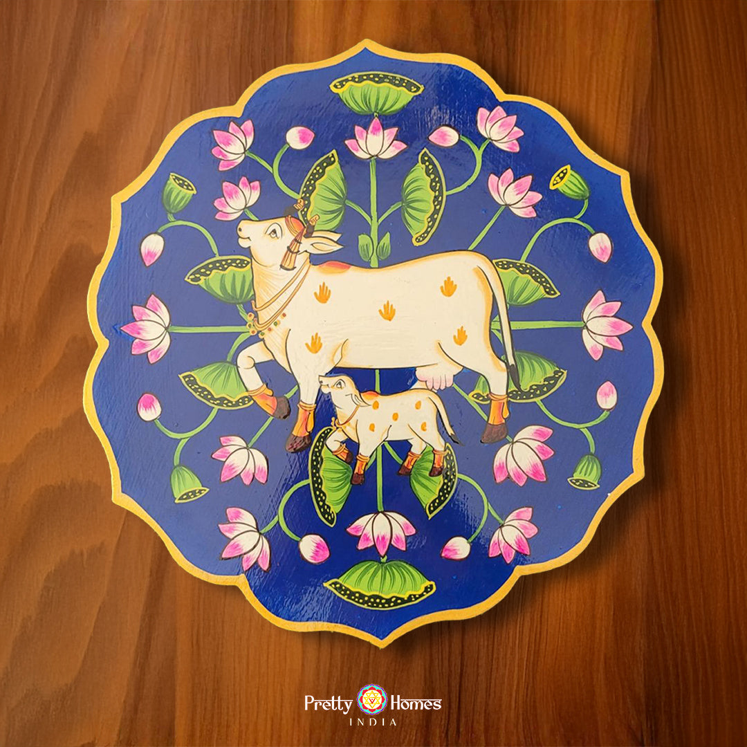 Blue petal-shaped wooden wall plate featuring pichwai cow and calf surrounded by lotus motifs. Pichwai wall art for spiritual settings.