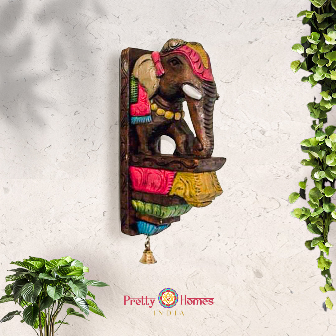 Hand-painted multicolored wooden elephant wall sconce with carved saddle and small hanging brass bell.