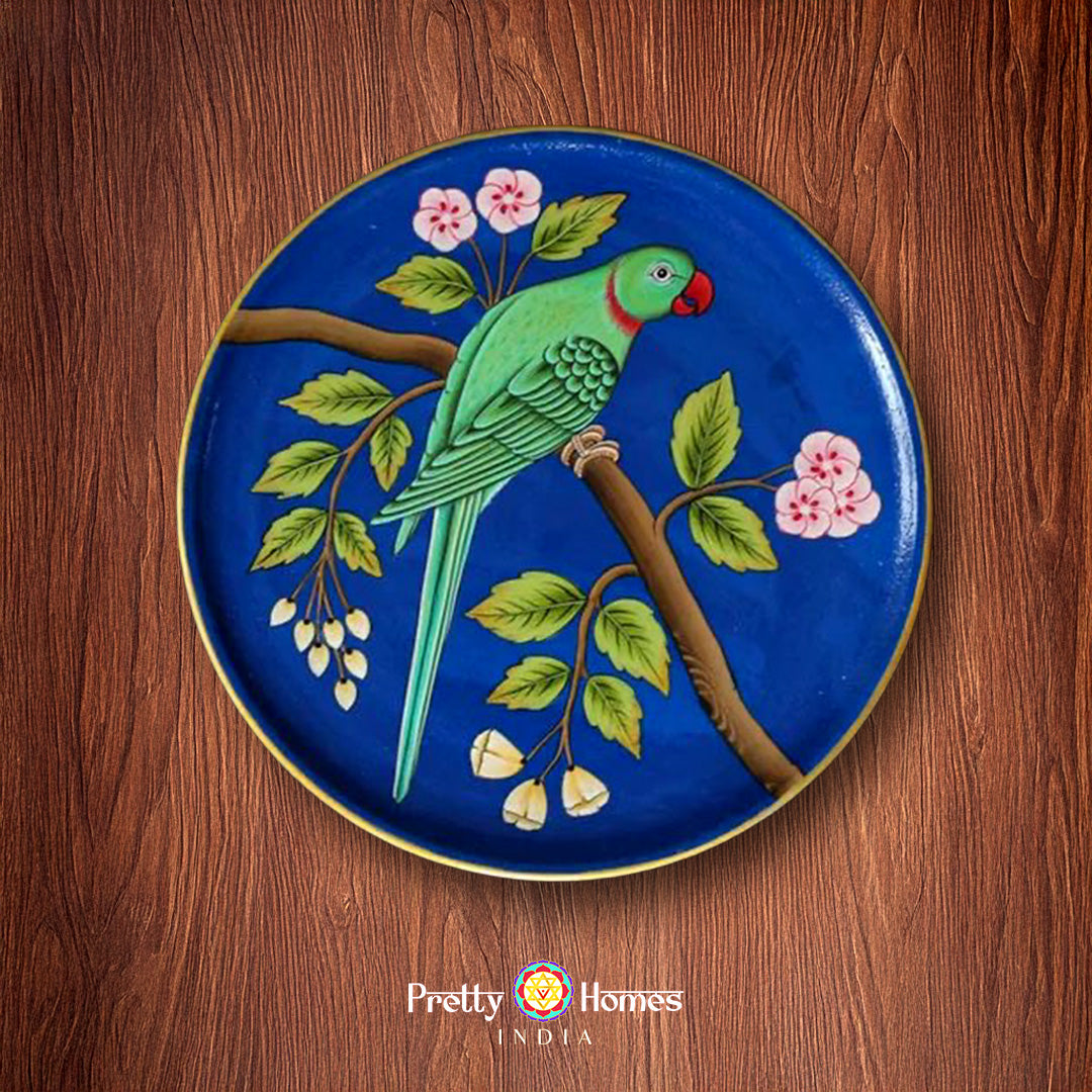 Handpainted wall plate with green parrot perched on flowering tree branch, deep blue background.