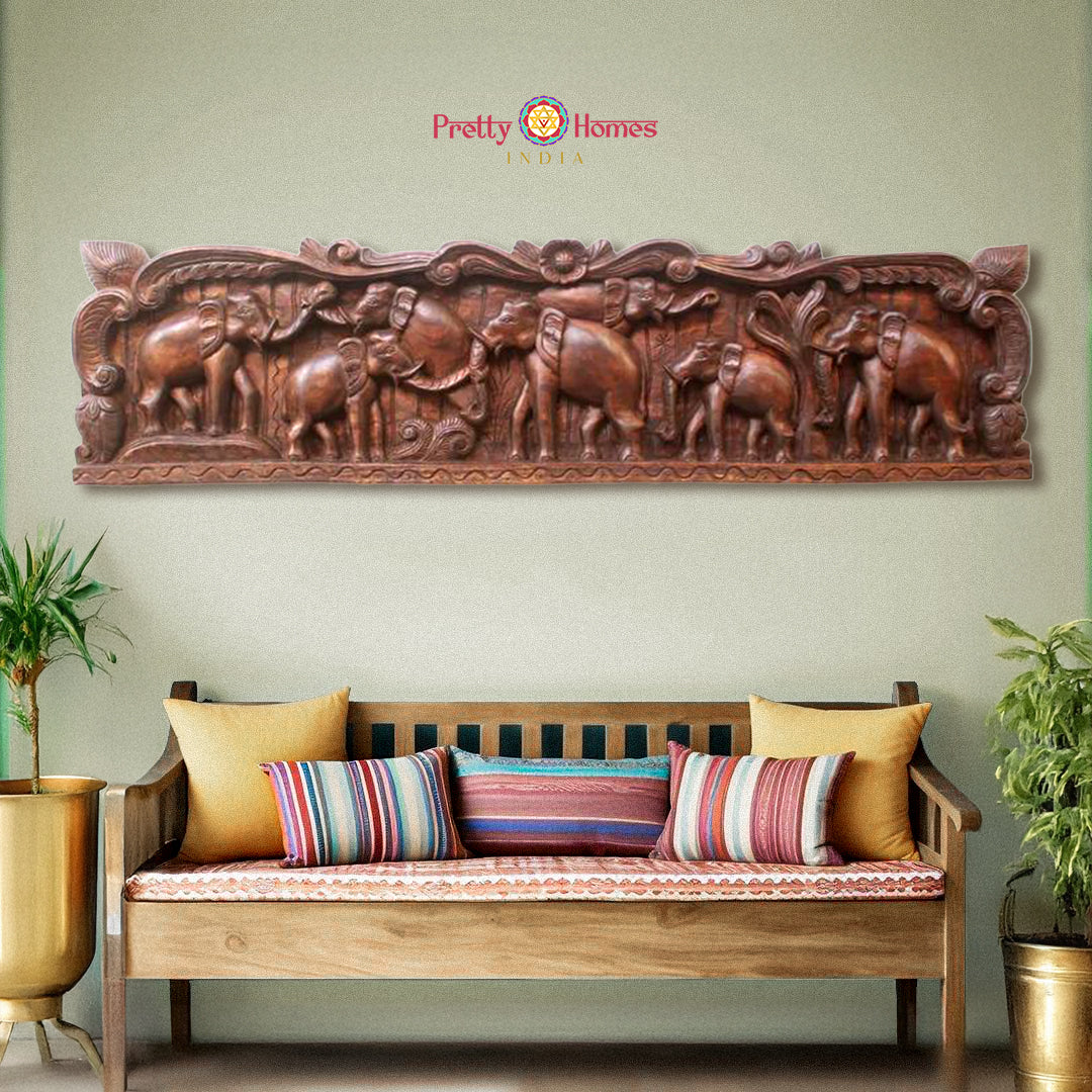A wall-mounted wooden elephant sculpture in a vintage finish, positioned above a bench with cushions in a home setting.