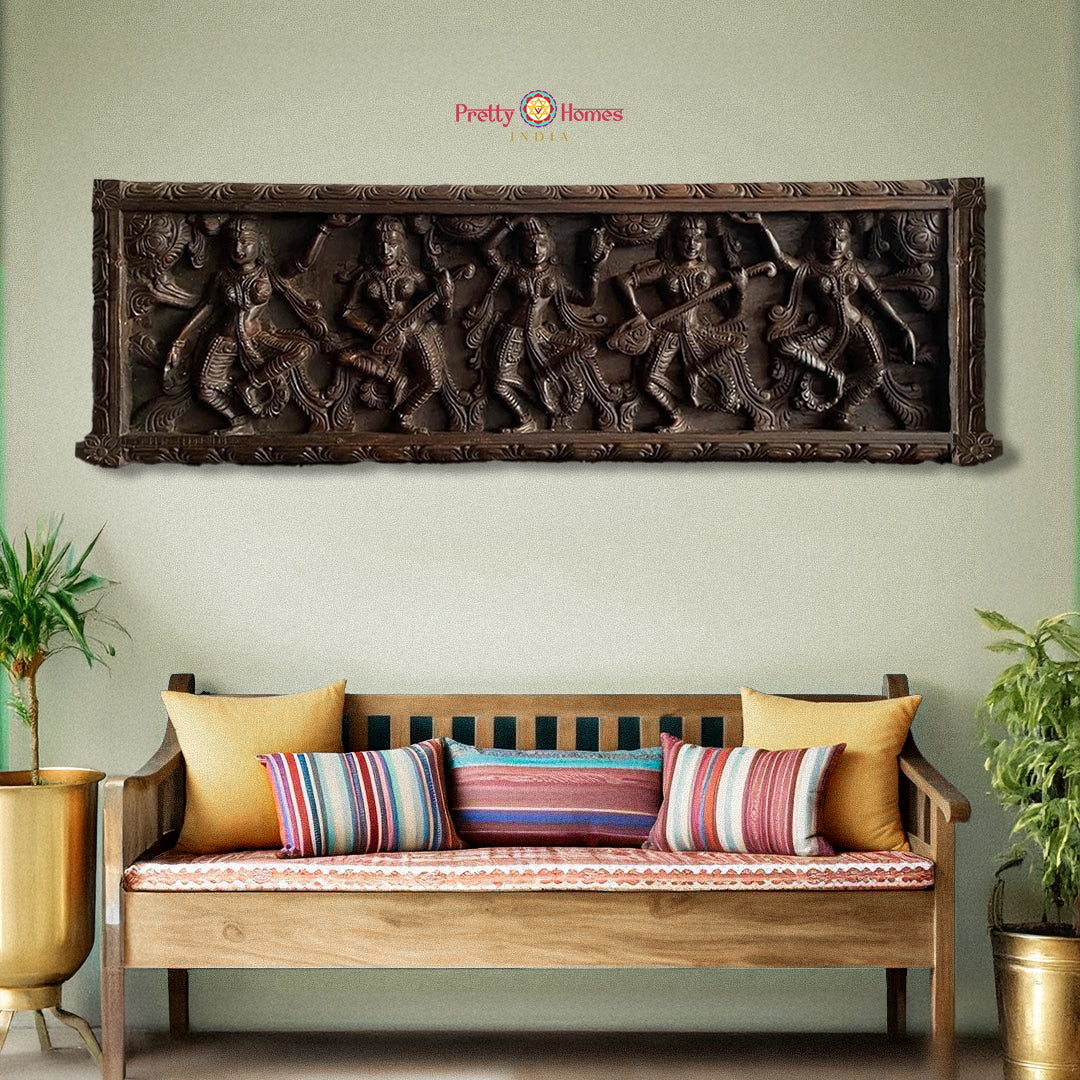 A woodcarved panel featuring a group of Apsaras, or divine damsels, playing musical instruments, mounted on a wall above a bench with cushions.