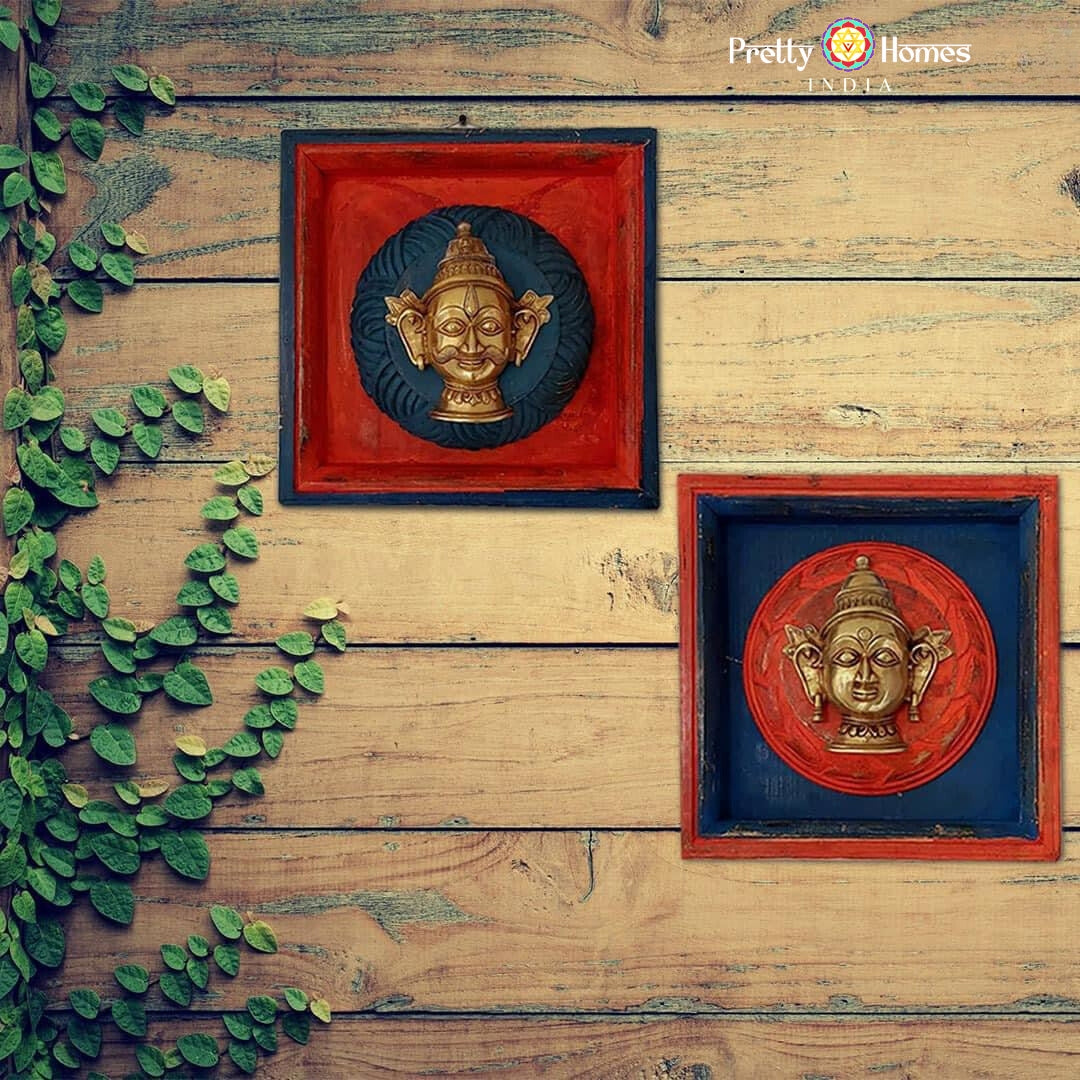 Two square wooden shadowbox frames with small brass visage masks mounted on rustic plank background.