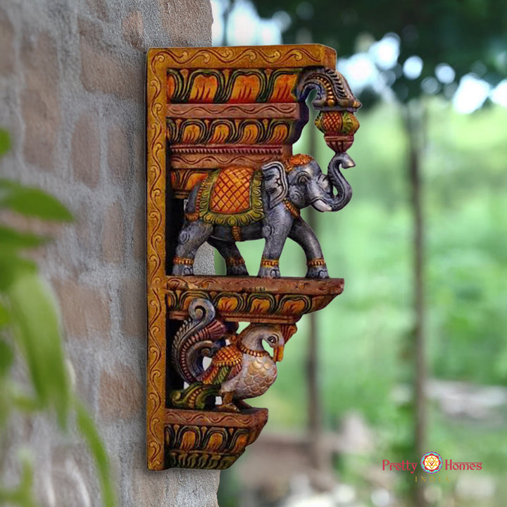 Decorative wall shelf with elephant and peacock design on a stone wall. “18 inch trunk up elephant wooden wall bracket with peacock design”