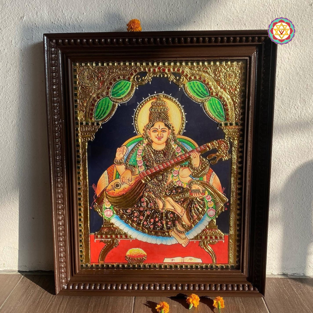 “Saraswati Tanjore painting placed in real room lighting, highlighting traditional frame and shine”