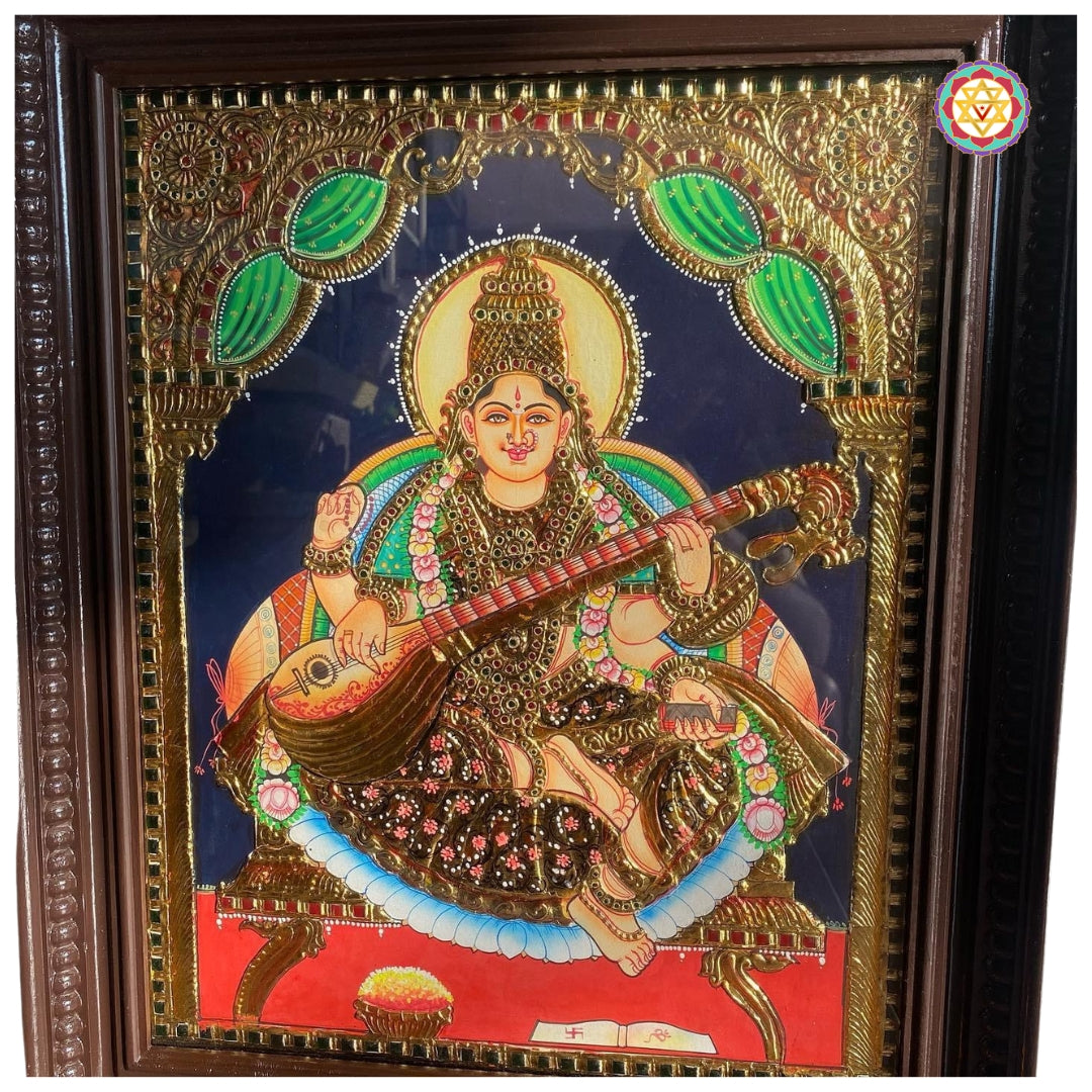 “Saraswati Tanjore painting showing goddess seated with veena in vibrant red and blue background”