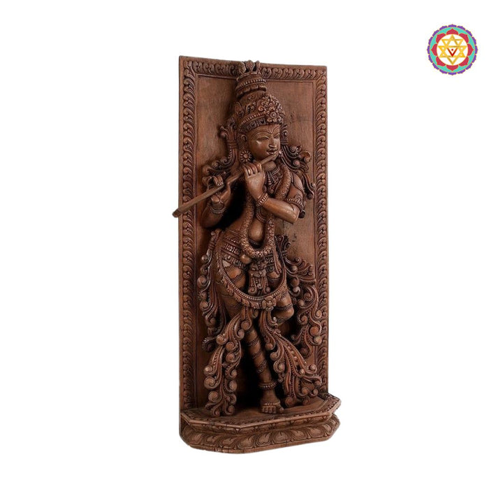 Decorative wall panel with a carved figure of a deity on a white background - Side view of Krishna wall hanging with floral carvings

