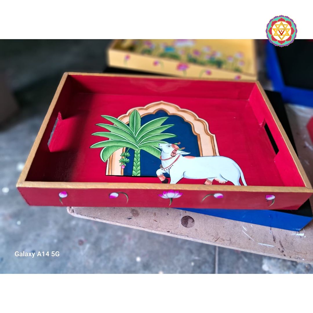 Angled view of red Pichwai tray showing cow and tree artwork on wood.