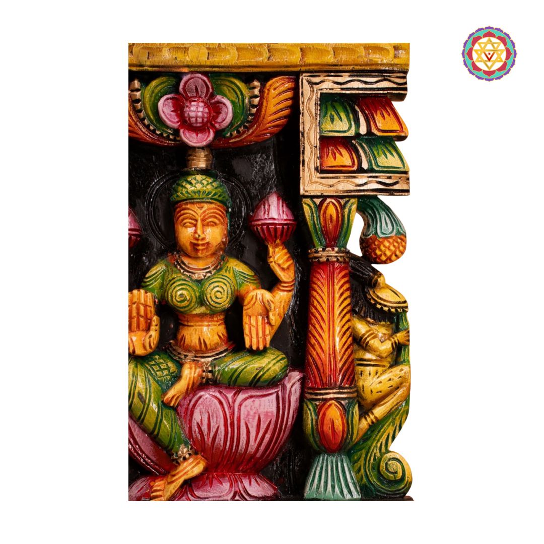 Colorful decorative wall piece with a seated figure and architectural elements on a white background: Close-up of Goddess Laxmi seated in carved temple frame
