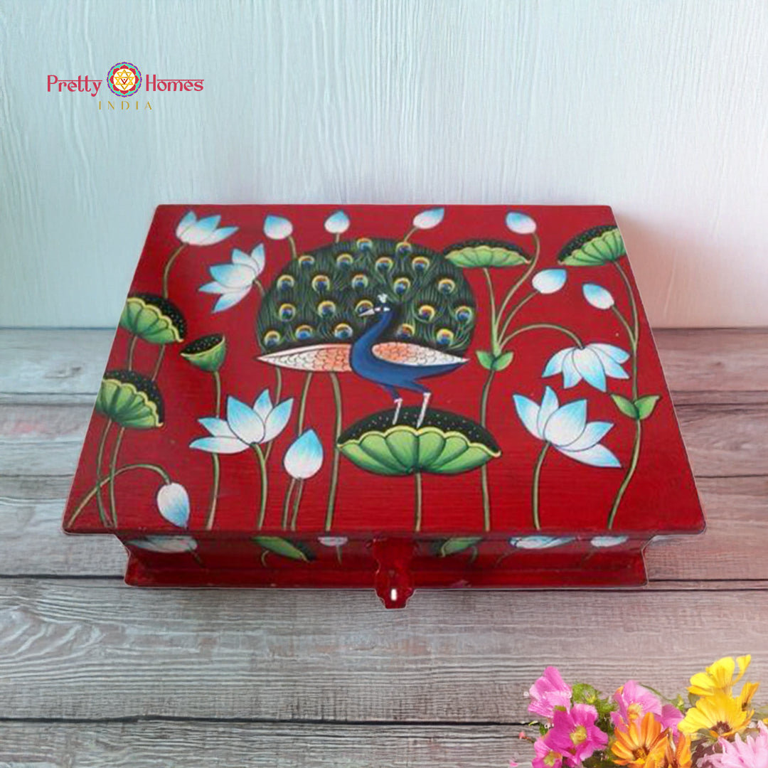 Medium red wooden Pichwai box with hand-painted peacock and lotus artwork, placed on a light wooden surface.