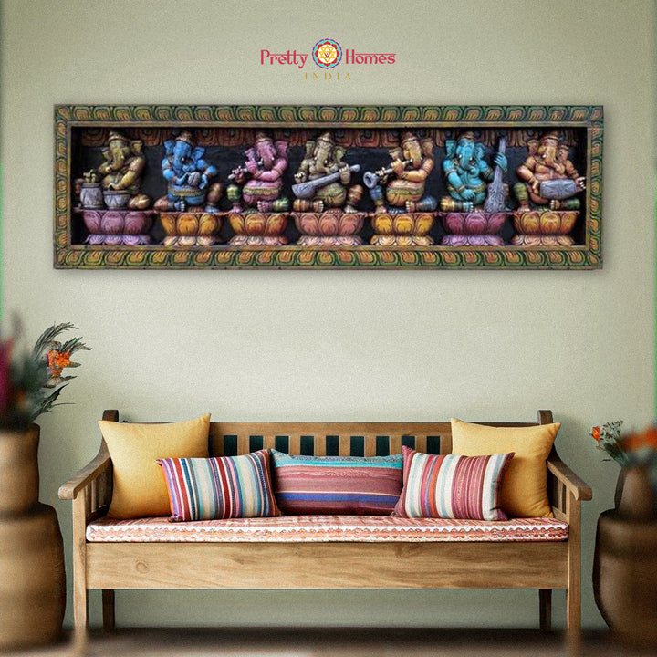 A hand-carved wooden panel depicting multiple images of Lord Ganesha playing musical instruments, displayed on a wall above a bench with cushions.