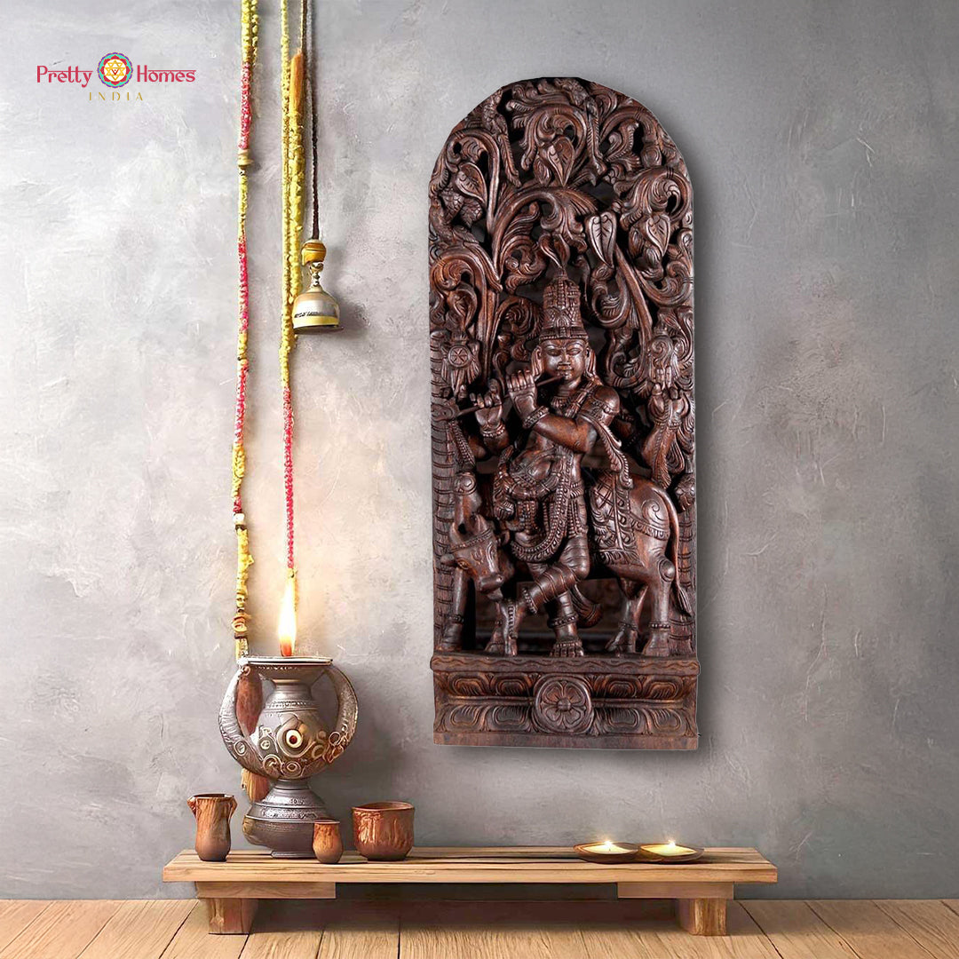 Front view of wooden Lord Krishna statue standing under carved canopy with sacred cow behind