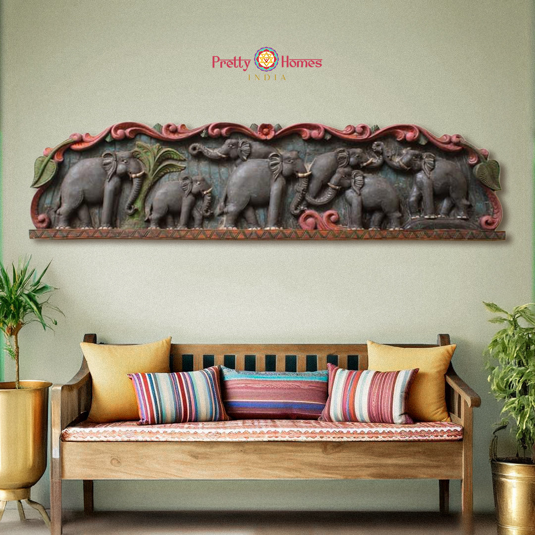 A wall-mounted wooden panel with a vintage finish featuring carved elephant figures in various poses, placed above a sofa with cushions in a living room setting.