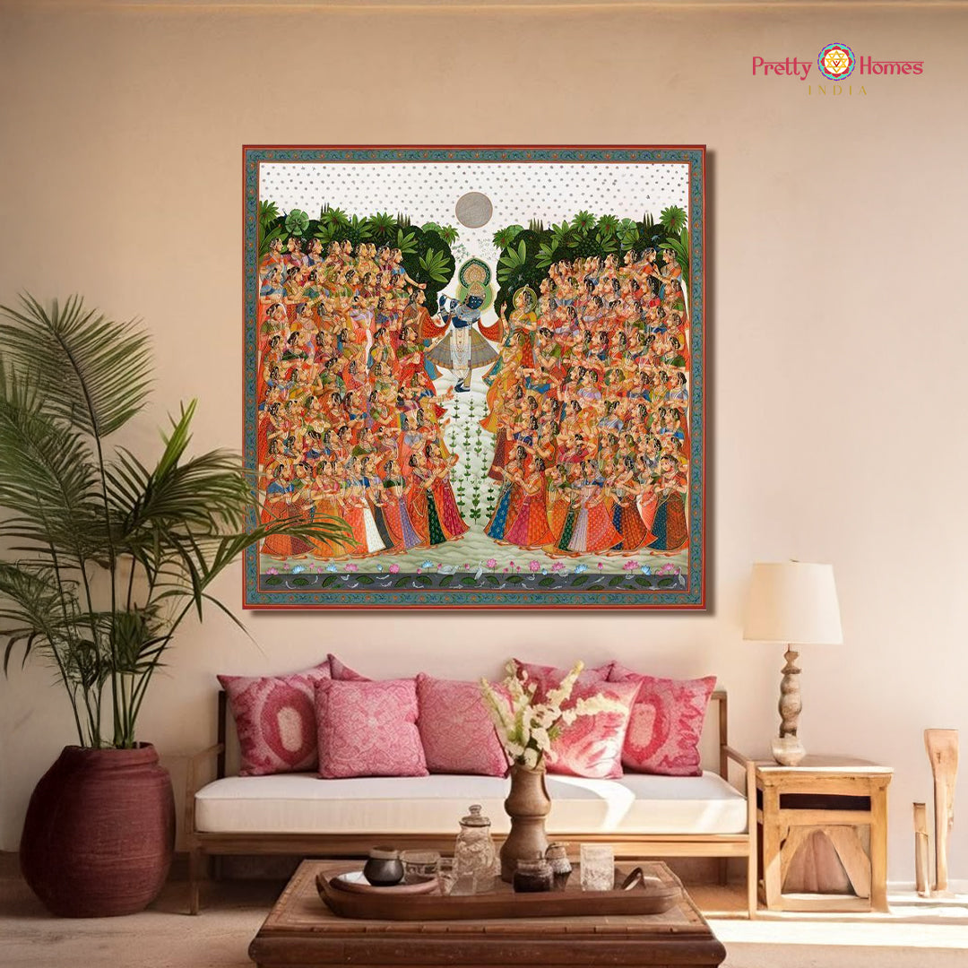 Hand-painted pichwai of Krishna playing flute, surrounded by Gopikas in colorful attire, displayed in a cozy living room.