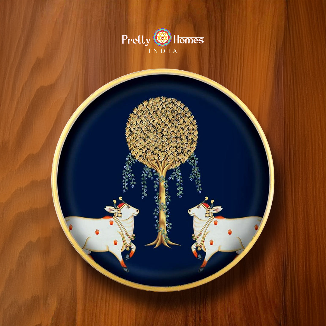 12-inch round wooden Pichwai wall plate featuring two white cows under golden Kalpavruksha tree on dark blue base. Ideal for Pichwai home decor.