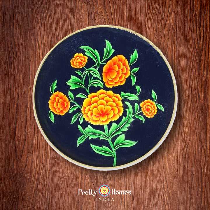 Handpainted pichwai wall plate with marigold flowers on a deep blue base, placed on wooden background.