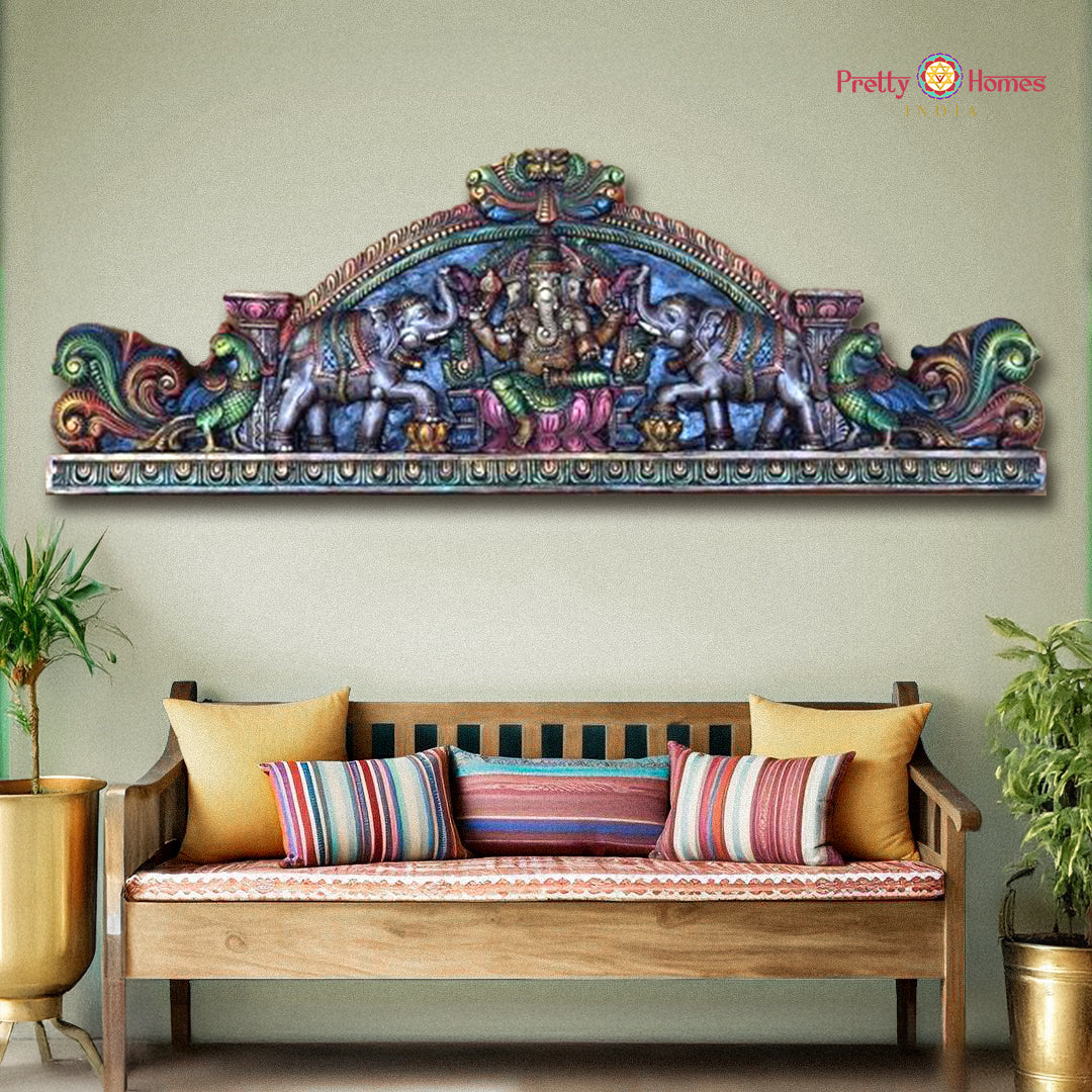 Decorative wall art above a wooden bench with colorful cushions, against a light green wall. Horizontal wooden wall panel with Ganesha, peacocks, parrots, and Yali

