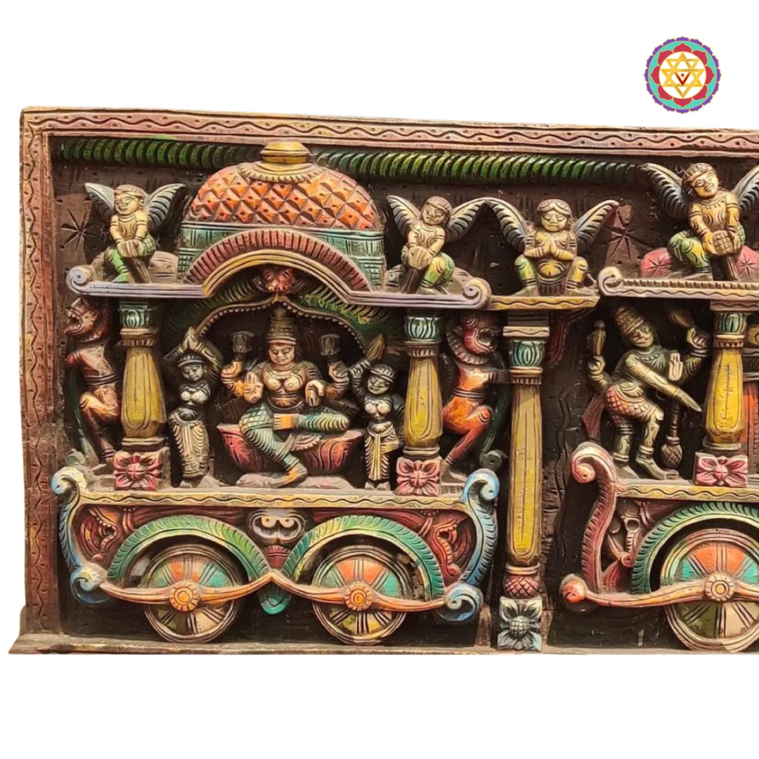 hand-carved wooden wall panel showing lord ganesha goddess lakshmi and goddess saraswati seated together on a decorative chariot with ornate background details