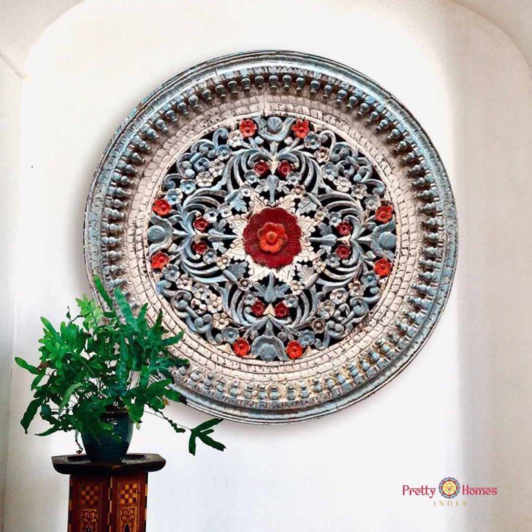 A hand-carved wooden jali wall panel with a distressed painted finish in blue, white, and red, mounted on a wall.