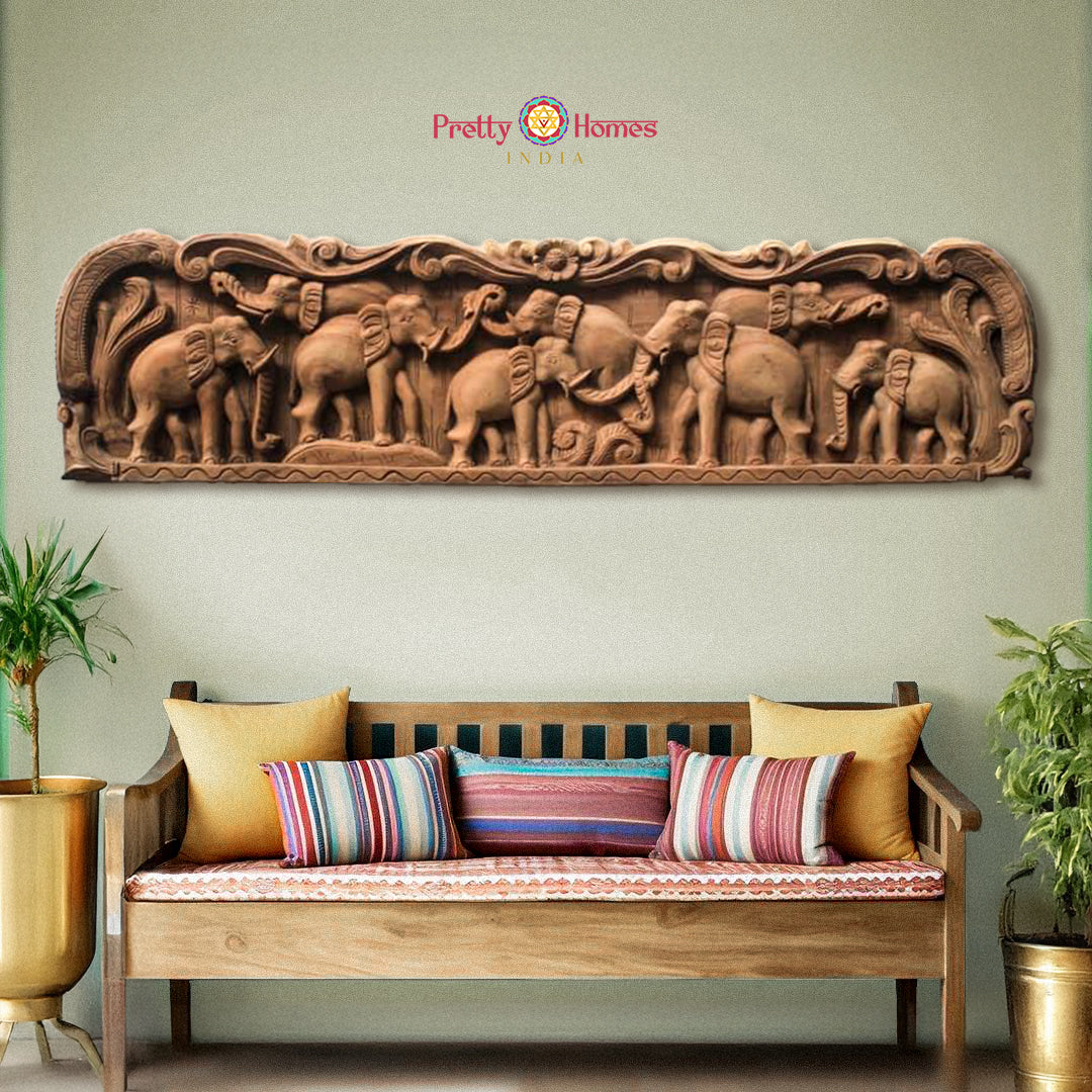 A wall-mounted wooden panel with a vintage finish featuring carved elephant designs, placed above a sofa with cushions in a living room setting.
