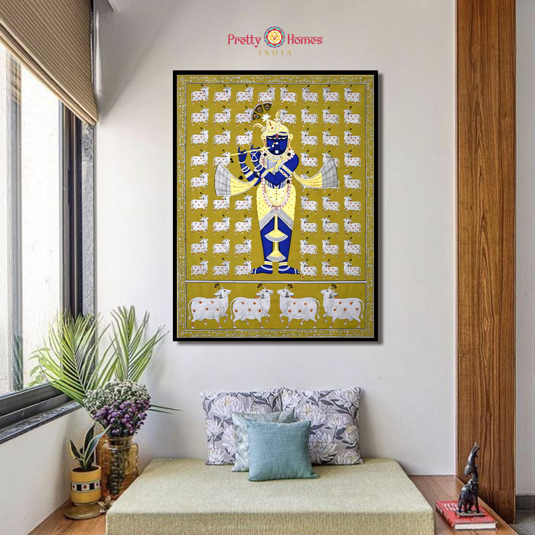 Hand-painted pichwai of Srinathji with flute and cows on mustard background, displayed in a modern room.