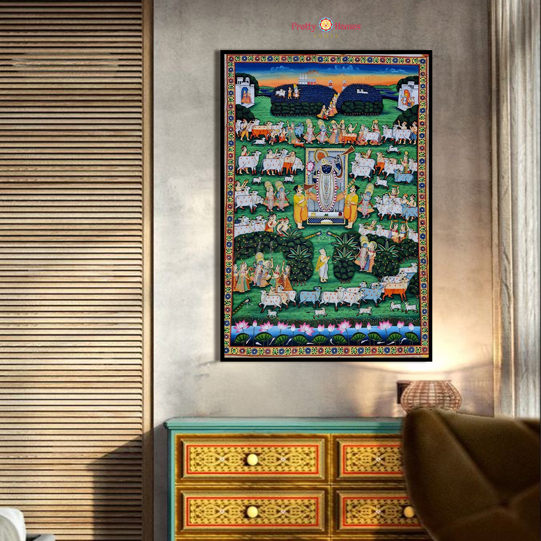 Hand-painted pichwai of Srinathji with gods and cows, lush green fields, displayed in a cozy room.