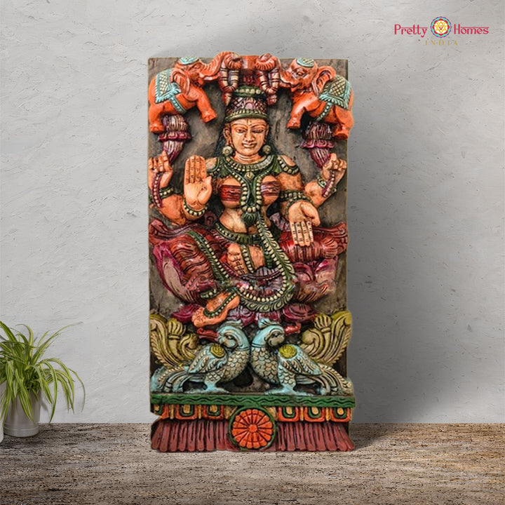 A vertically oriented, intricately carved wooden panel featuring the goddess Gajalakshmi with elephants and peacocks, in multicolor finish. Vertical Gajalakshmi wooden panel with peacocks and elephants

