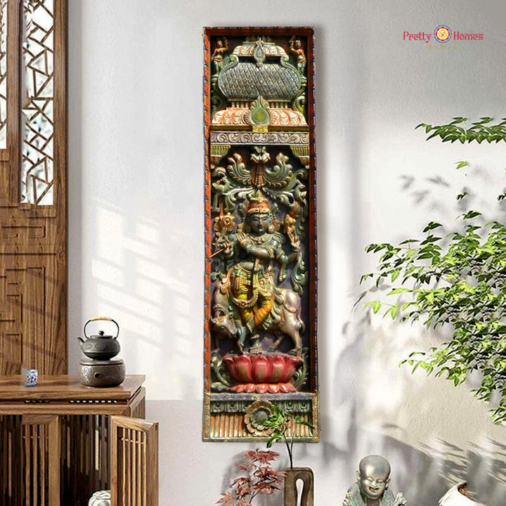 Decorative wall panel with intricate carvings in a room with plants and wooden furniture. Vertical wooden wall panel with Krishna and cows in vintage finish

