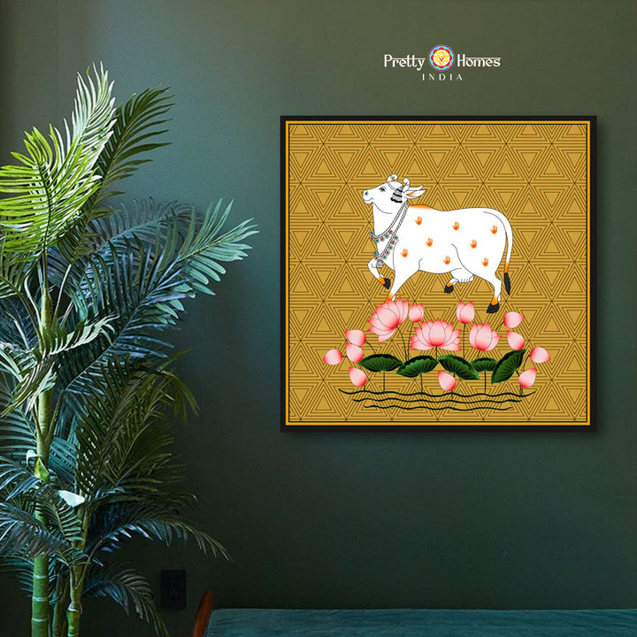 Hand-painted pichwai of sacred white cow standing on pink lotuses, displayed on mustard background in a modern interior.