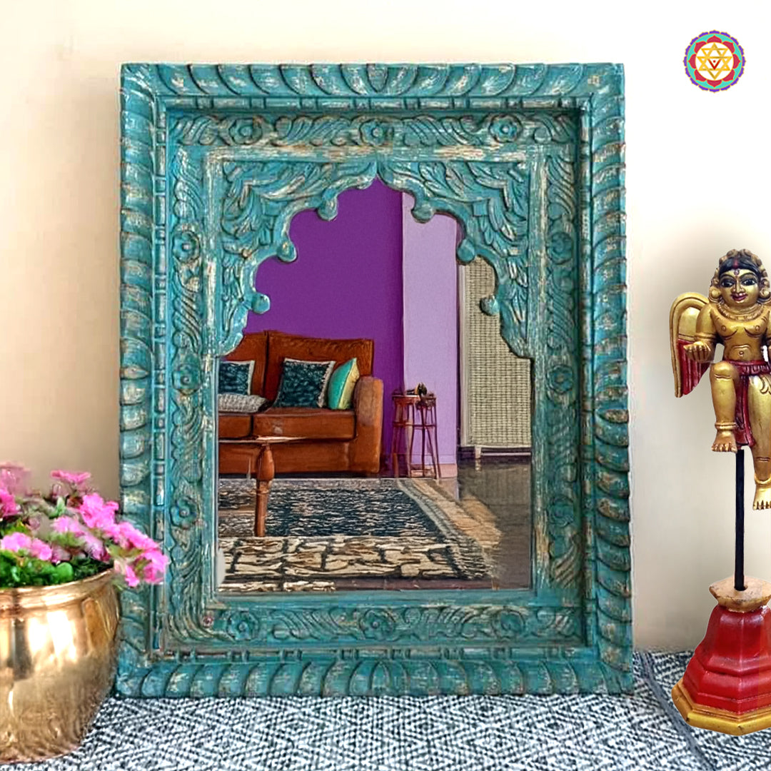“Rustic turquoise wooden Jharokha mirror frame placed in a living room, showcasing its intricate floral carving.”