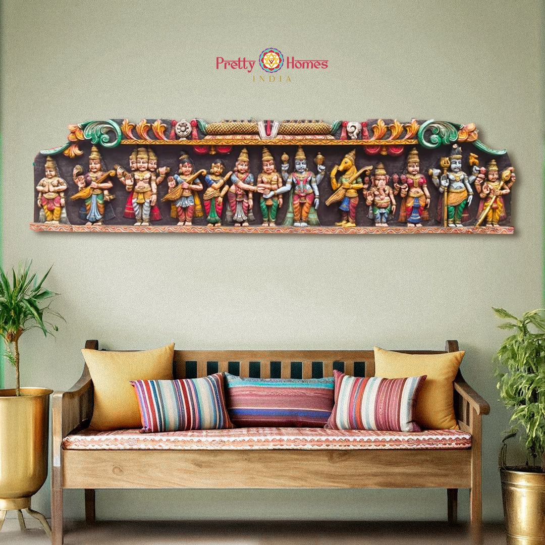 A hand-carved wooden wall panel depicting a mythological wedding scene with various characters in colorful attire, placed above a bench with cushions.