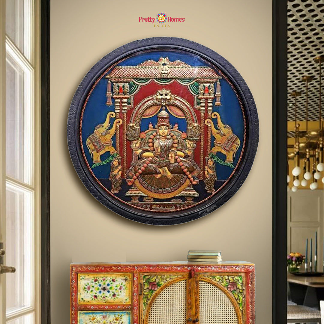 “Round Gajalakshmi Tanjore painting in carved teakwood frame displayed on an interior wall”