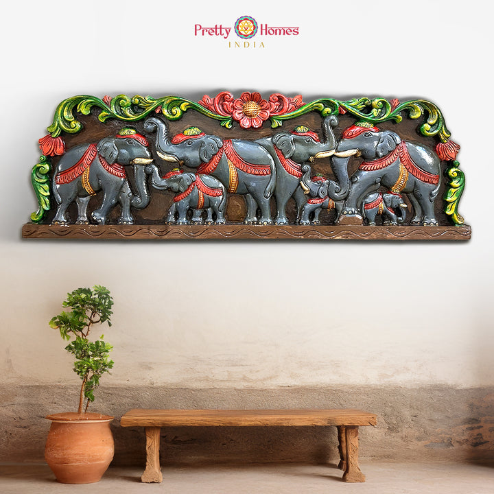 A woodcarved elephant wall panel with floral designs, in multicolour finish, displayed above a bench against a wall. - Elephant wooden wall panel with floral carvings in multicolour finish

