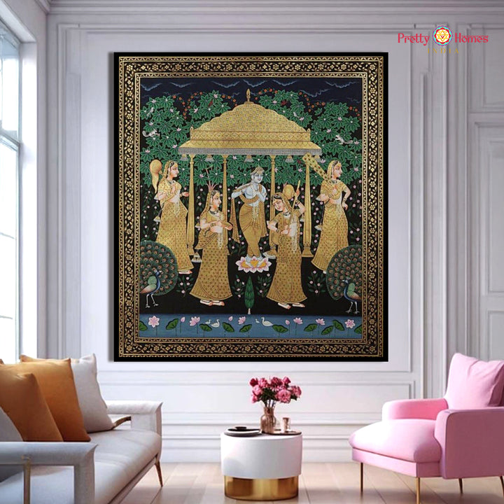 Hand-painted pichwai of Krishna with Gopikas playing music, golden pavilion, and peacocks, displayed in a bright modern living room.