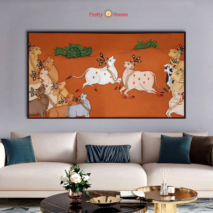 Hand-painted vintage style pichwai of cows, terracotta background, in a living room.

