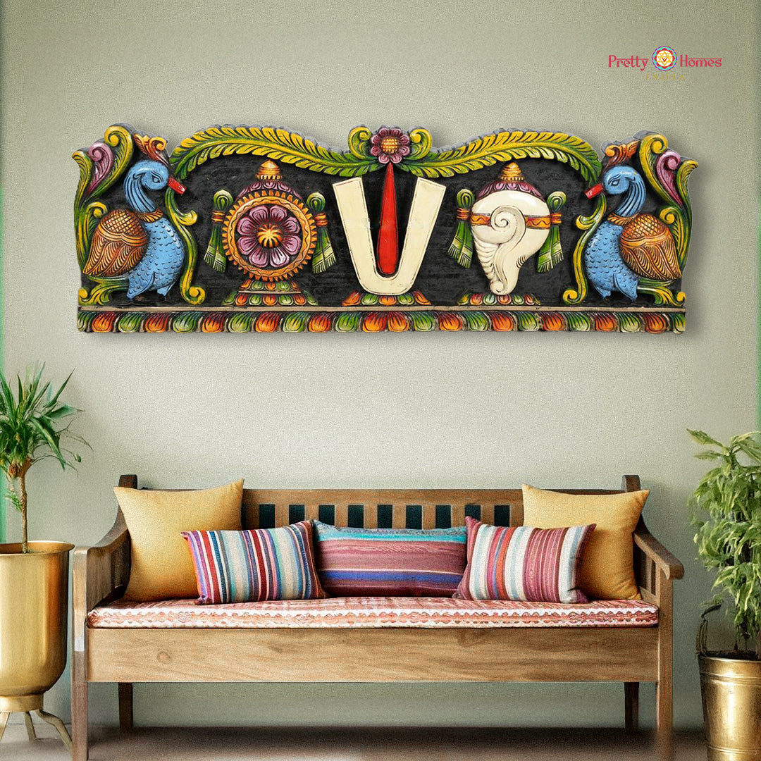 A wall-mounted wood carved panel featuring Hindu deity Venkateswara with a shankh and chakra, with hamsa and floral carvings, displayed above a bench with cushions.
