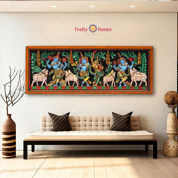 A horizontal wood-carved wall panel depicting Radha and Venugopal Krishna with cows, displayed above a sofa in a room with a light-colored wall.