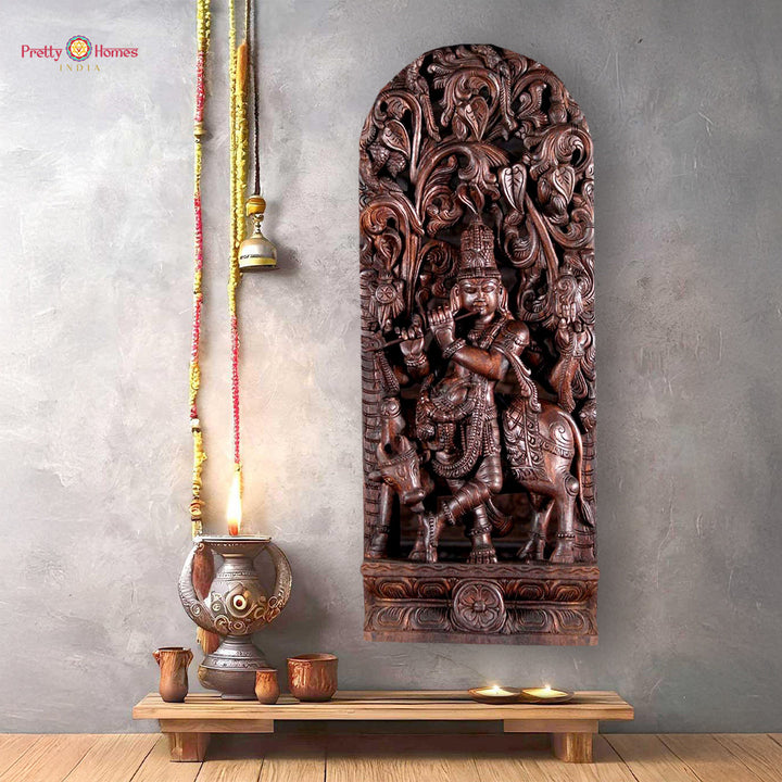 Wooden sculpture of Lord Krishna standing under a canopy with cow