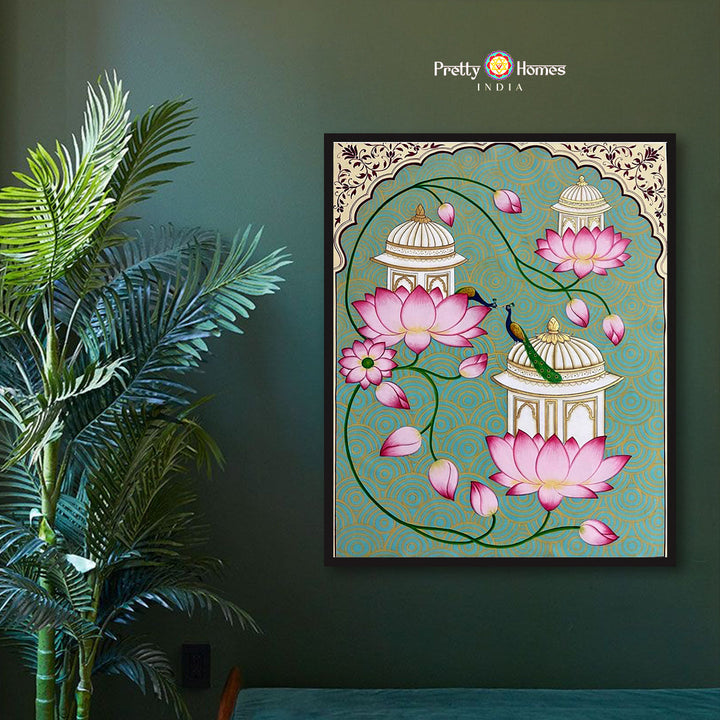 Hand-painted pichwai of garden pavilion with peacock and blooming lotuses, framed and displayed on green wall.