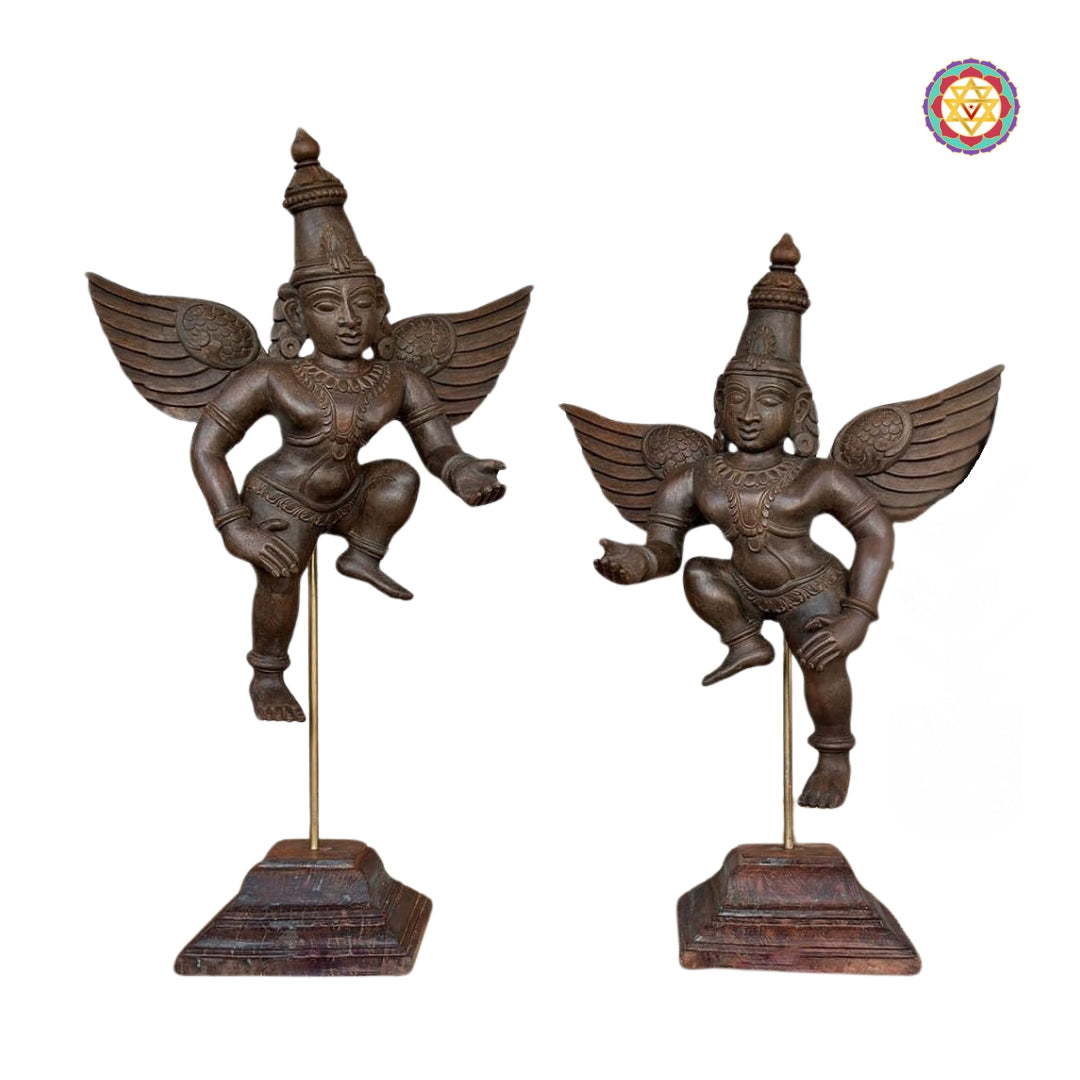 Front view of two hand-carved Gandharva wooden sculptures on metal stands — vintage polish and detailed feather carving